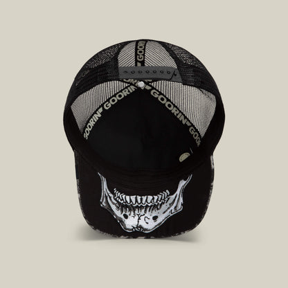 The Goorin Bros. Bone Head Unalive trucker hat, shown from above, features a black mesh back for breathable, all-day comfort and style. An open adjustable strap ensures a customizable fit, while a striking white skeleton jaw graphic decorates the underside of the brim.