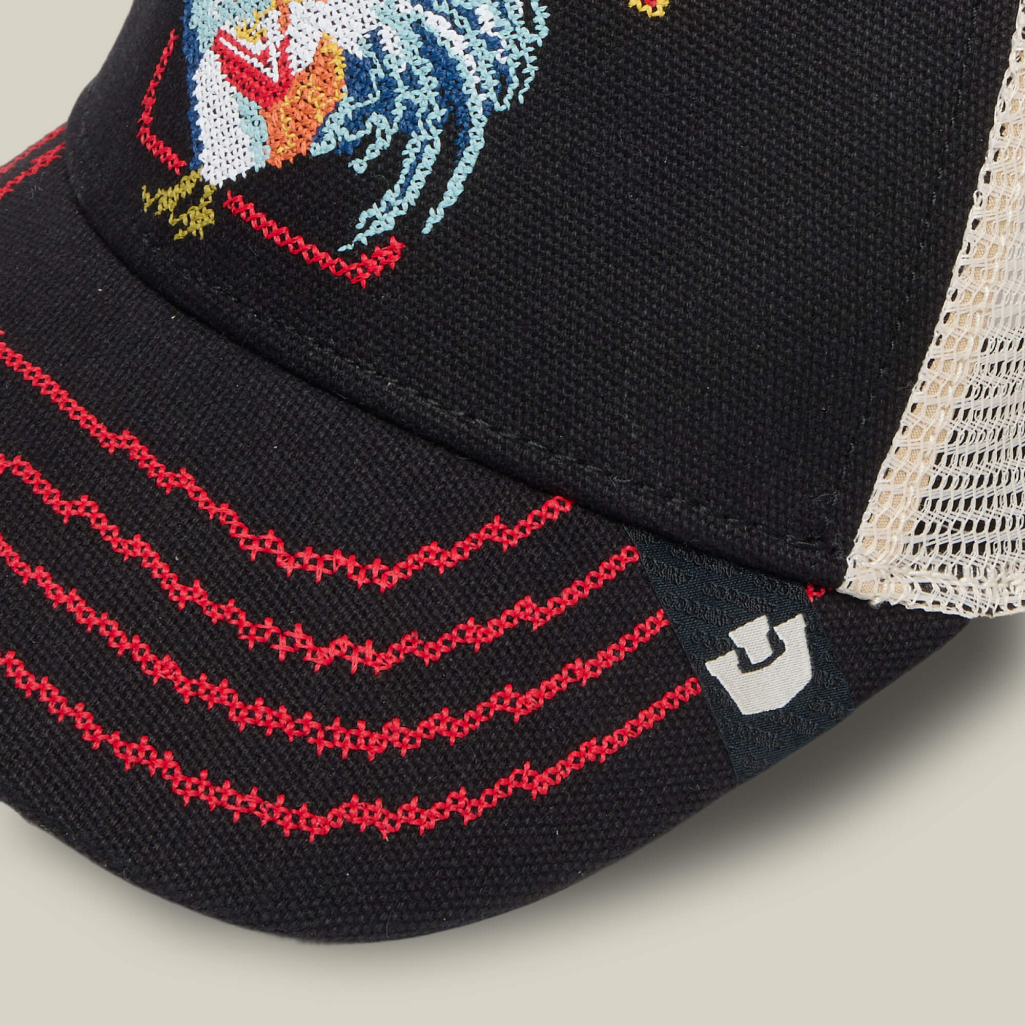 Close-up of the Goorin Bros. "Middle of No Where" black mesh trucker hat with red stitching, rooster embroidery, metallic logo on the brim, and subtle nods to classic home cookin’ and fried chicken style.