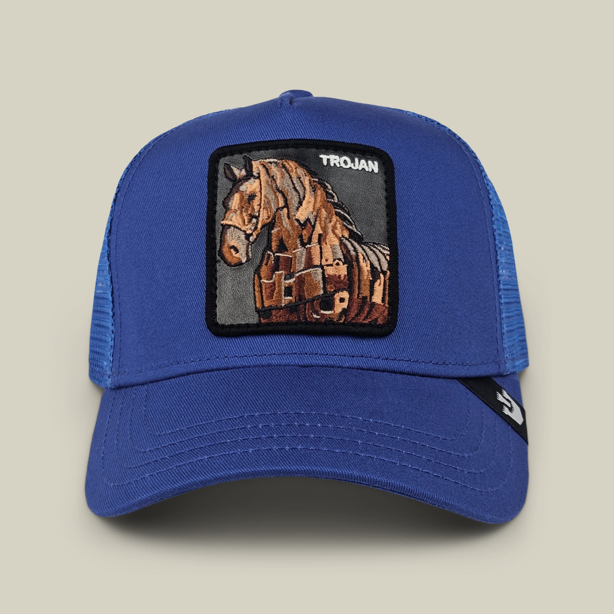The Goorin Bros. 99 Strong is a royal blue trucker hat featuring a mesh back panel and embroidered trojan horse patch on the front, displayed against a neutral background.