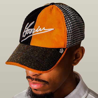 A man wearing the Goorin Bros. "South Bay" Papa cap, a multicolored patchwork hat with textured houndstooth, orange and brown panels, featuring Goorin Script embroidery and a small logo tag on the side.