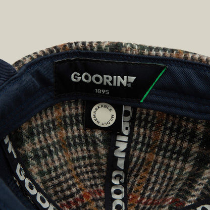 Close-up of the inside of a six-panel Cozy Tailored Baseball cap by Goorin Bros., featuring the “Goorin 1895” brand label, a “Remarkable Mind” pin, and plaid inner lining.