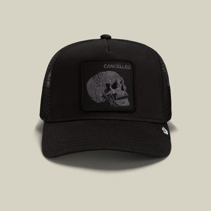 The Goorin Bros. Tonal Skull trucker hat features a black mesh back with a solid black front panel displaying a gray skull patch embossed with "Cancelled" text, shown against a neutral background.