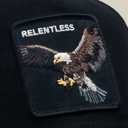 The Goorin Bros. Suede Relentless Eagle Trucker is a navy trucker hat featuring an embroidered eagle patch with yellow accents and "Relentless" text on dark suede fabric, shown in close-up detail.