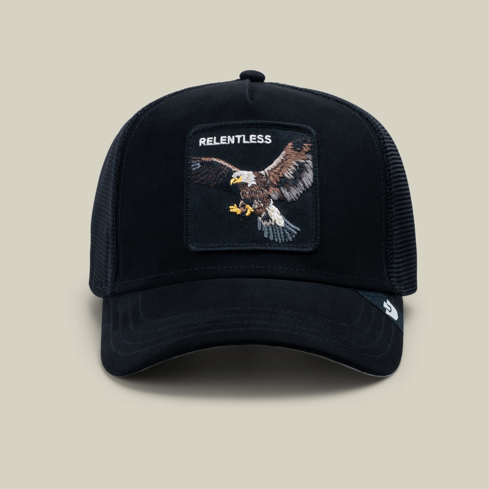 The Goorin Bros. Suede Relentless Eagle Trucker in Void features a black suede-feel brim, breathable mesh back, and a patch with an embroidered bald eagle topped by the word “RELENTLESS,” showcased against a plain light background.