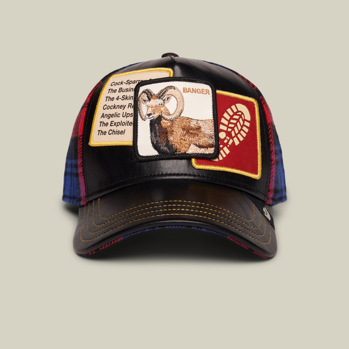 The Goorin Bros. Banger trucker hat features a black front panel with an embroidered ram patch labeled "Banger," navy and red plaid sides, gold accents, and a dark brown bill, displayed on a neutral background.