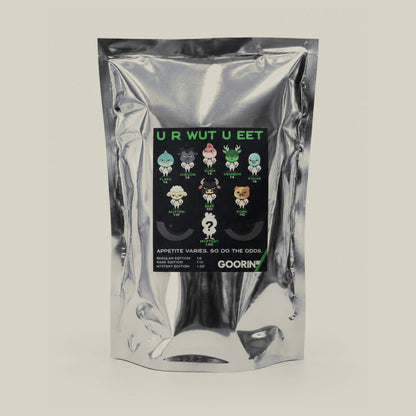 A multi-color silver foil bag with a black label featuring cartoon characters teases Goorin Bros.’ Blind Box 1: U R WUT U EET, with product details below the art for a fun blind box experience.