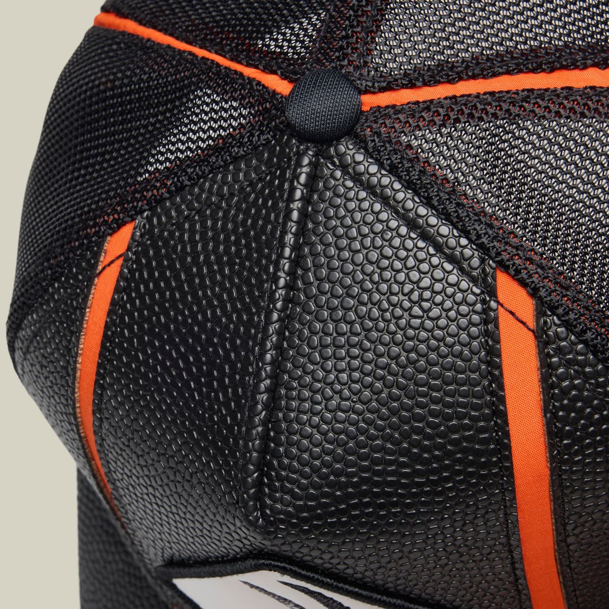 The Goorin Bros. Know Ball baseball cap features black breathable mesh with orange fabric accents and a textured black rubber patch detail on the crown, shown in a close-up product shot.