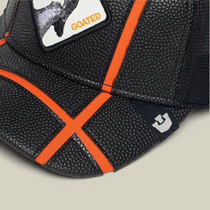 The Goorin Bros. Know Ball features a black coated mesh construction with bright orange trim and an X-pattern strap detail, shown in a close-up studio shot highlighting its textured grip surface.