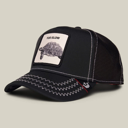 Black mesh-back cap from Goorin Bros. called "Down Low..." featuring a zigzag stitched brim and a front patch with a tortoise and the text TOO SLOW—a true badge of honor for those who embrace taking life at their own pace.