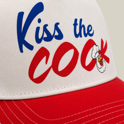 Close-up of a red and white Goorin Bros. cap called Chef's Kiss, featuring "Kiss the Cook" in blue and red letters with a cartoon chicken head—ideal for any backyard barbecue or aspiring grillmaster.