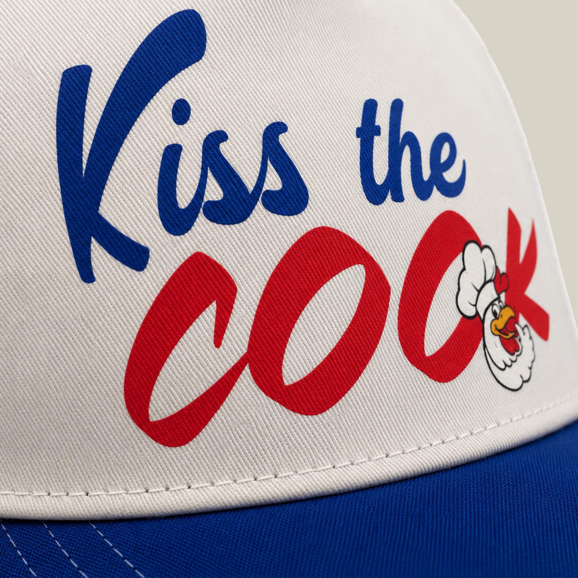 A close-up of the Chef's Kiss white and blue hat from Goorin Bros., featuring "KISS THE COOK" and a cartoon chicken in a chef's hat—ideal for any grillmaster fired up to serve delicious food.