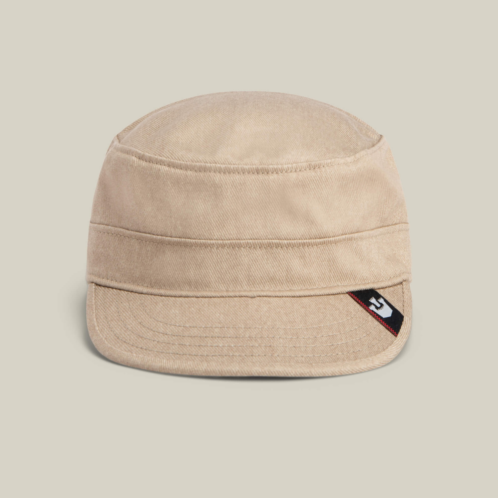 The Goorin Bros. "Home at Last" is a beige canvas military-style cap with a short brim, detailed with a small black, white, and red logo tag on the side, shown against a plain light background.