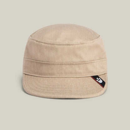 The Goorin Bros. "Home at Last" is a beige canvas military-style cap with a short brim, detailed with a small black, white, and red logo tag on the side, shown against a plain light background.