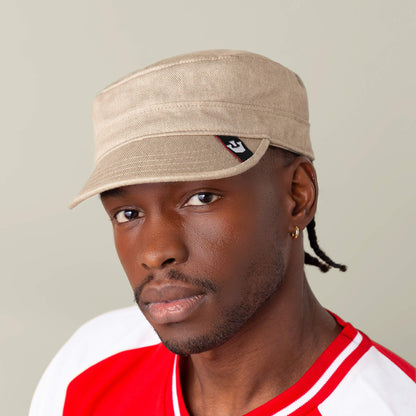 A man in the Goorin Bros. "Home at Last" tan cap and a red and white shirt looks at the camera against a plain background.