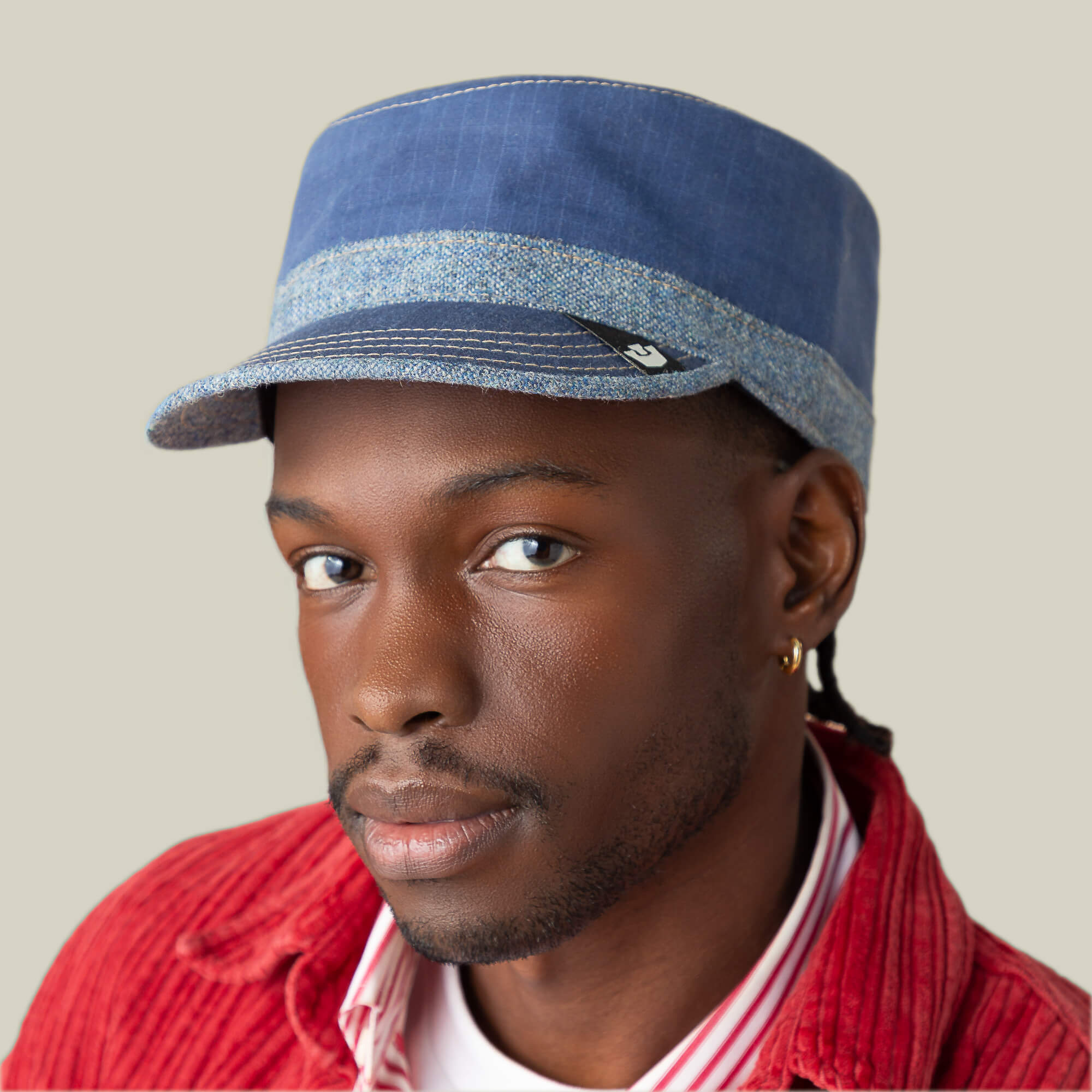 A person wearing the Goorin Bros. Ampere blue denim chambray hat, a red corduroy jacket, and a white-and-red striped shirt, looking at the camera against a plain background.