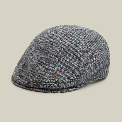 The Gibbins flatcap by Goorin Bros. in Oil Gray is displayed against a plain beige background. This men’s cap features a textured fabric with subtle multicolored flecks, adding refined detail to its timeless design.