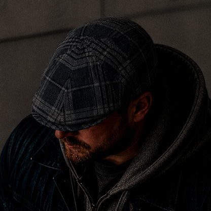 A man in the Glenwood Grove jacket by Goorin Bros., his face partially shadowed, head slightly bowed beneath the hoodie, wears a classic flatcap.