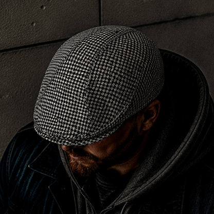 Wearing a Goorin Bros. Norwood classic flatcap in black and white houndstooth, a person in a dark jacket and hoodie bows their head to partially obscure their face.