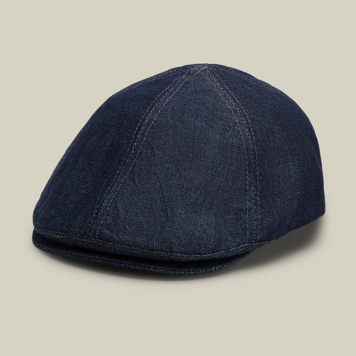 The Goorin Bros. Noisy Benjamin Paul flatcap in indigo features visible stitching and is displayed on a neutral beige background.