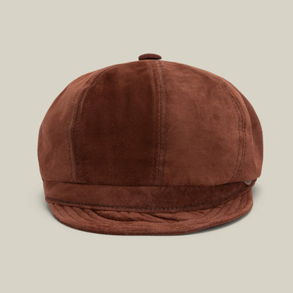 The Goorin Bros. Ruthy is a brown suede cabbie-style flatcap featuring visible stitching, a button top, and a short round brim, showcased against a plain beige background.