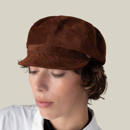 Person with short brown hair wears the Ruthy cabbie flatcap by Goorin Bros. and a white collared shirt, looking down against a plain light background.