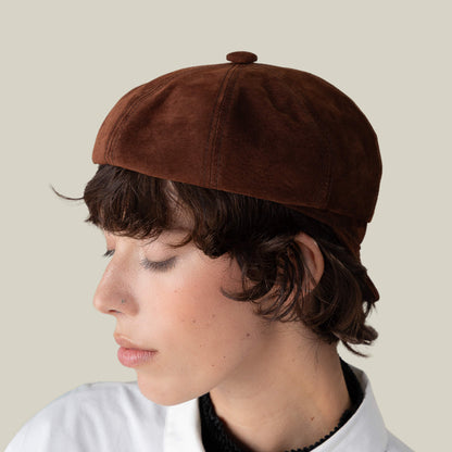 Person with short brown hair wears the Goorin Bros. Ruthy suede cabbie flatcap and a white collared shirt, facing left against a plain beige background.