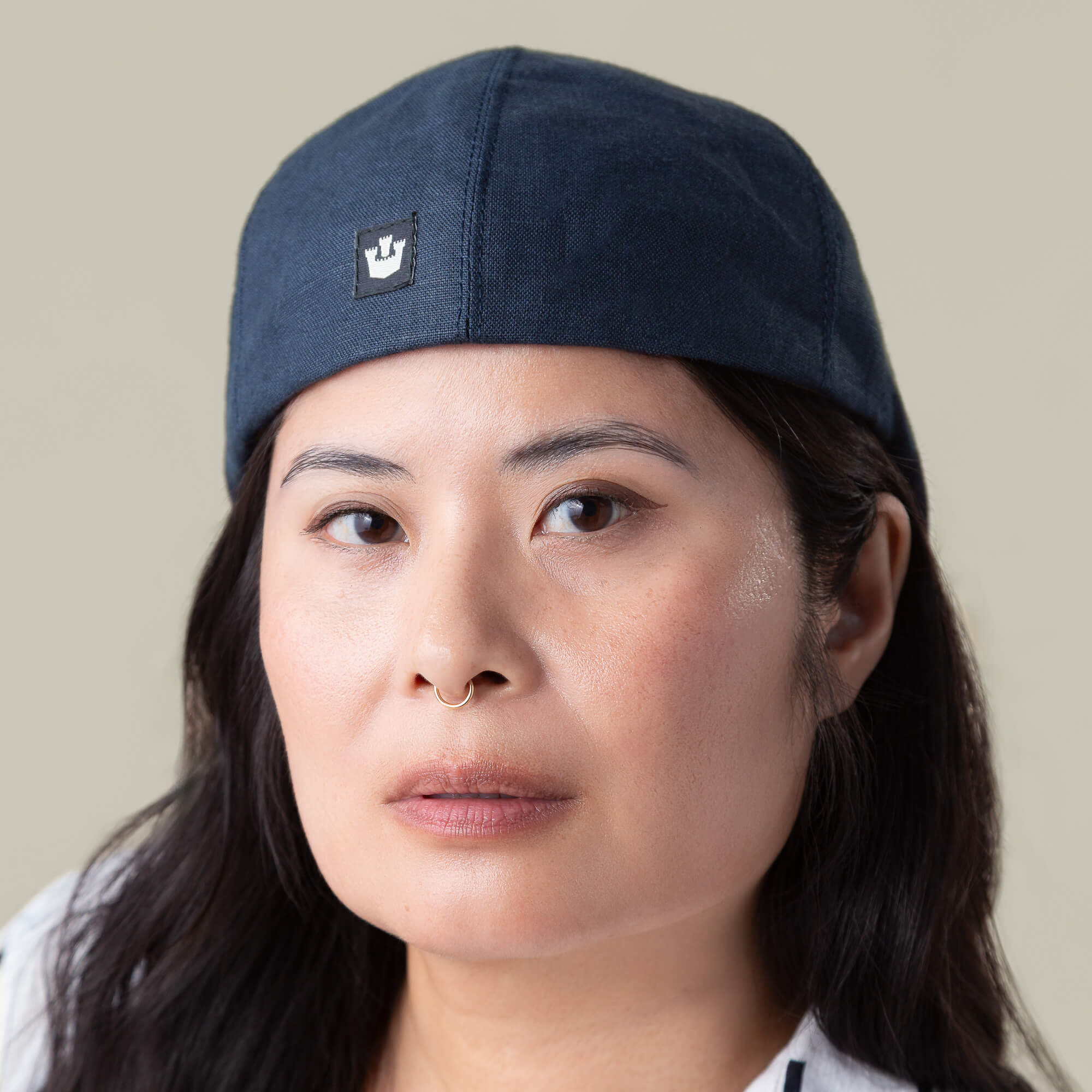 A person with long dark hair and a septum ring wears a navy blue Benjamin Paul six-panel hat from Goorin Bros., looking directly at the camera with a neutral expression.