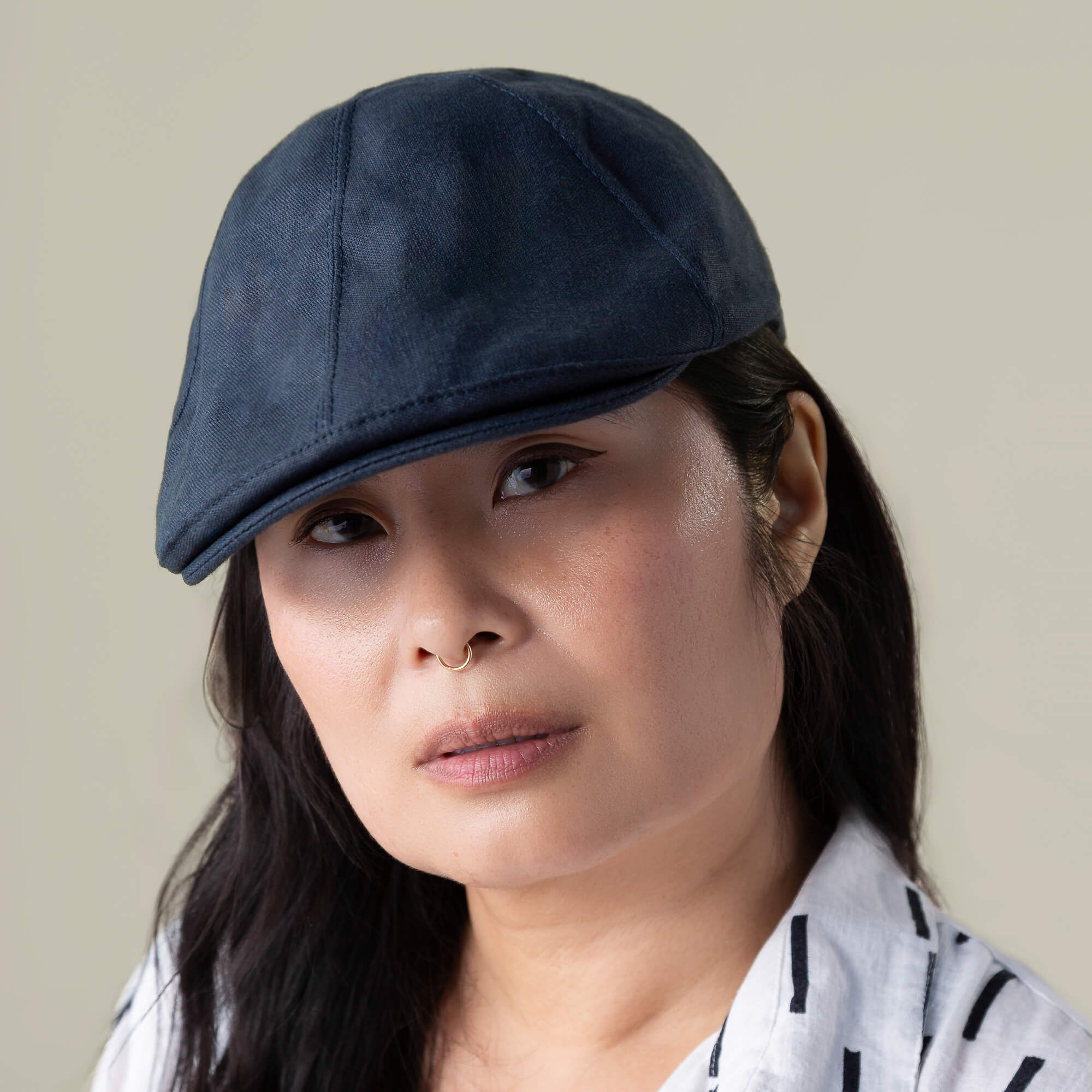 A person with long dark hair wears the Goorin Bros. Benjamin Paul blue six-panel hat and a white shirt with black stripes, looking at the camera with a neutral expression.