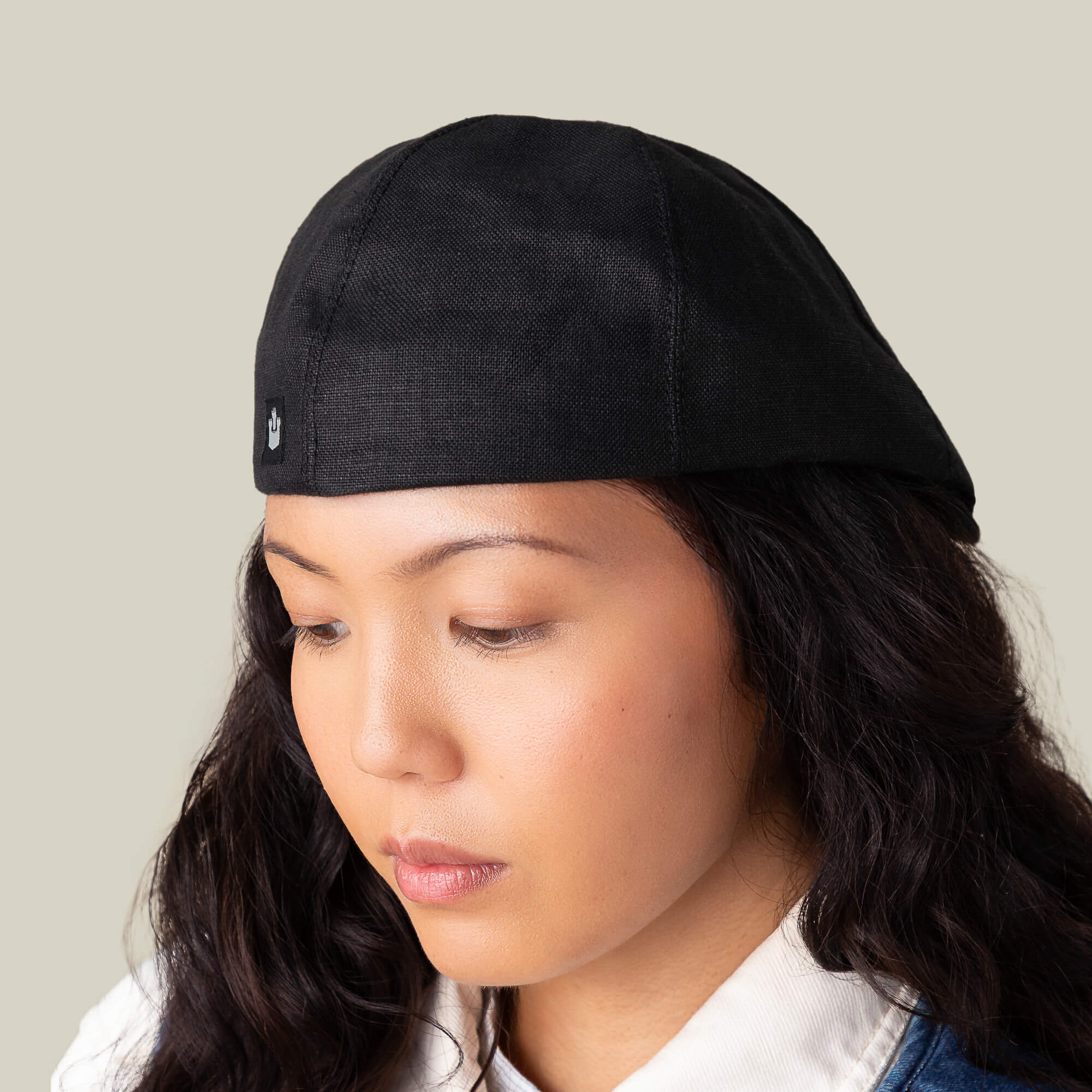 A person with long dark hair wears the Goorin Bros. Benjamin Paul black three-season hat and a white shirt, looking downward against a plain background.