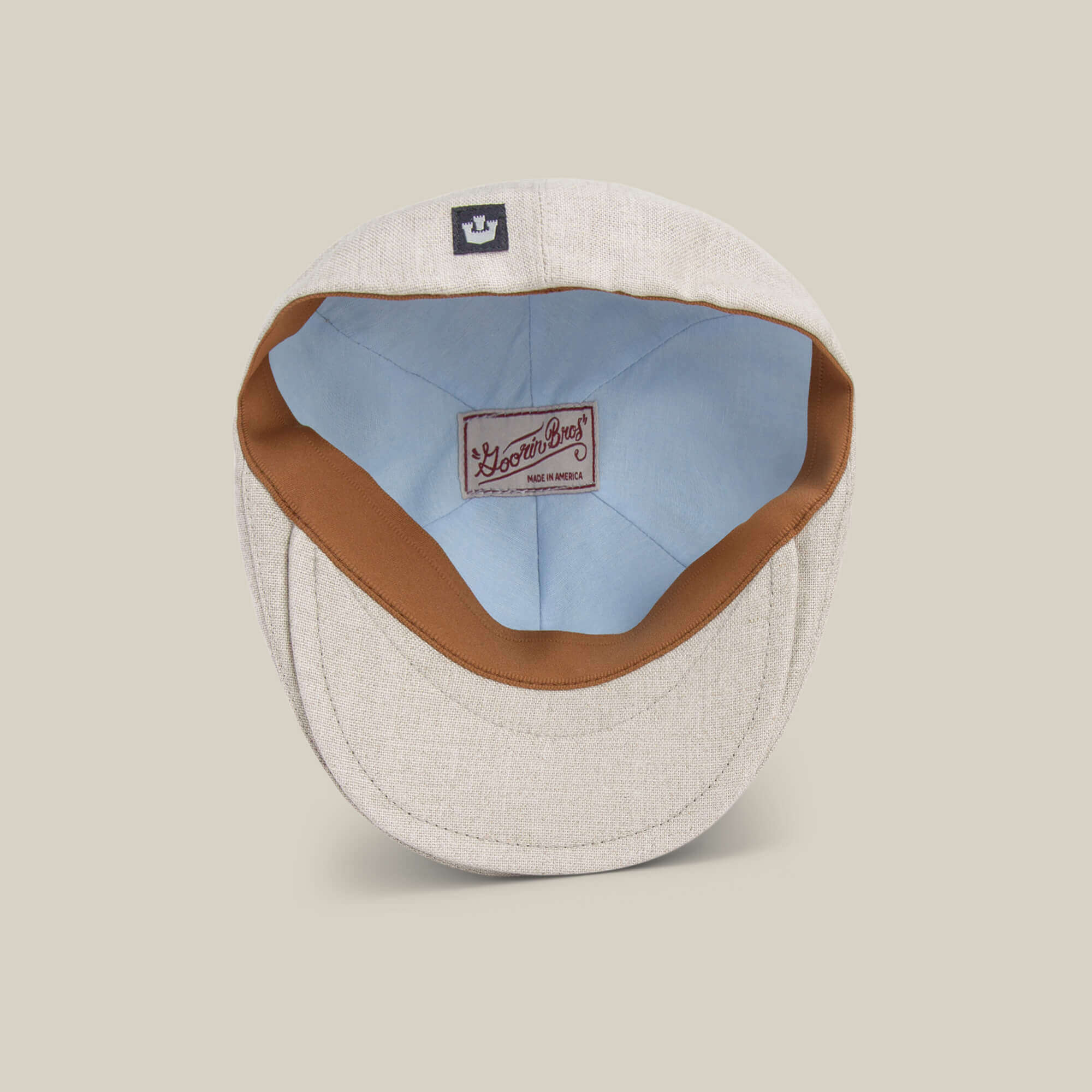 The Benjamin Paul by Goorin Bros. is a beige linen flat cap with a top view showing its light blue lining, brown sweatband, and two woven brand labels—a versatile three-season hat for daily wear.