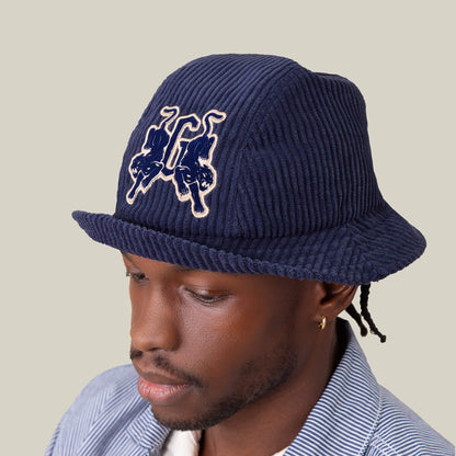 A man wears the Goorin Bros. "Yes Coach" navy ribs corduroy bucket hat with an embroidered front graphic and a striped button-up shirt, set against a plain background.