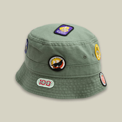 The Goorin Bros. PLU 1895 SHADE bucket hat features colorful embroidered patches on the top and sides, making it stand out like a walking bulletin board when displayed against a plain light background.