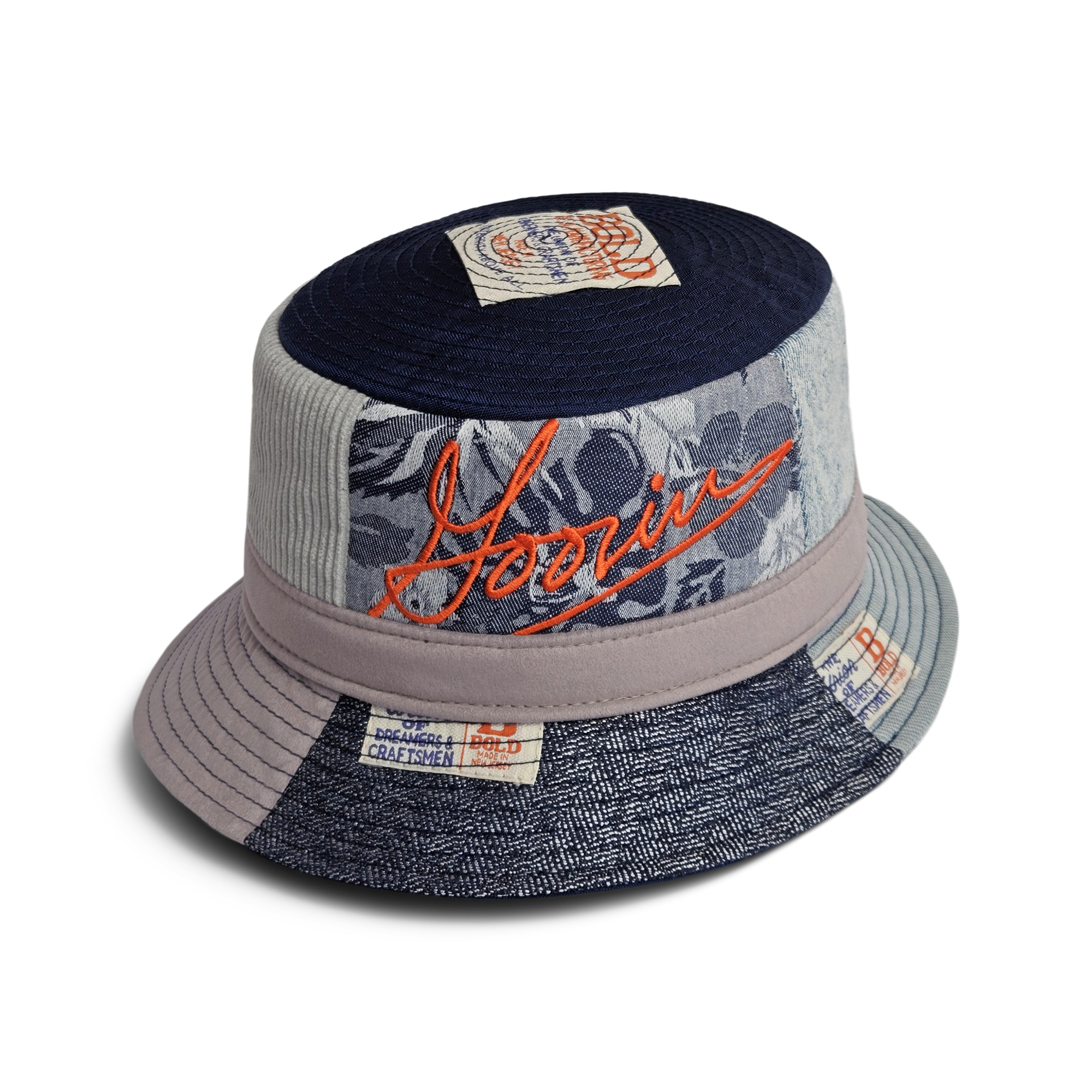 The Goorin Rework Bucket by Goorin Bros. features mixed denim and fabric panels, floral patchwork, an orange embroidered logo, assorted fabric labels, and recycled materials—an ideal Earth Day pick.