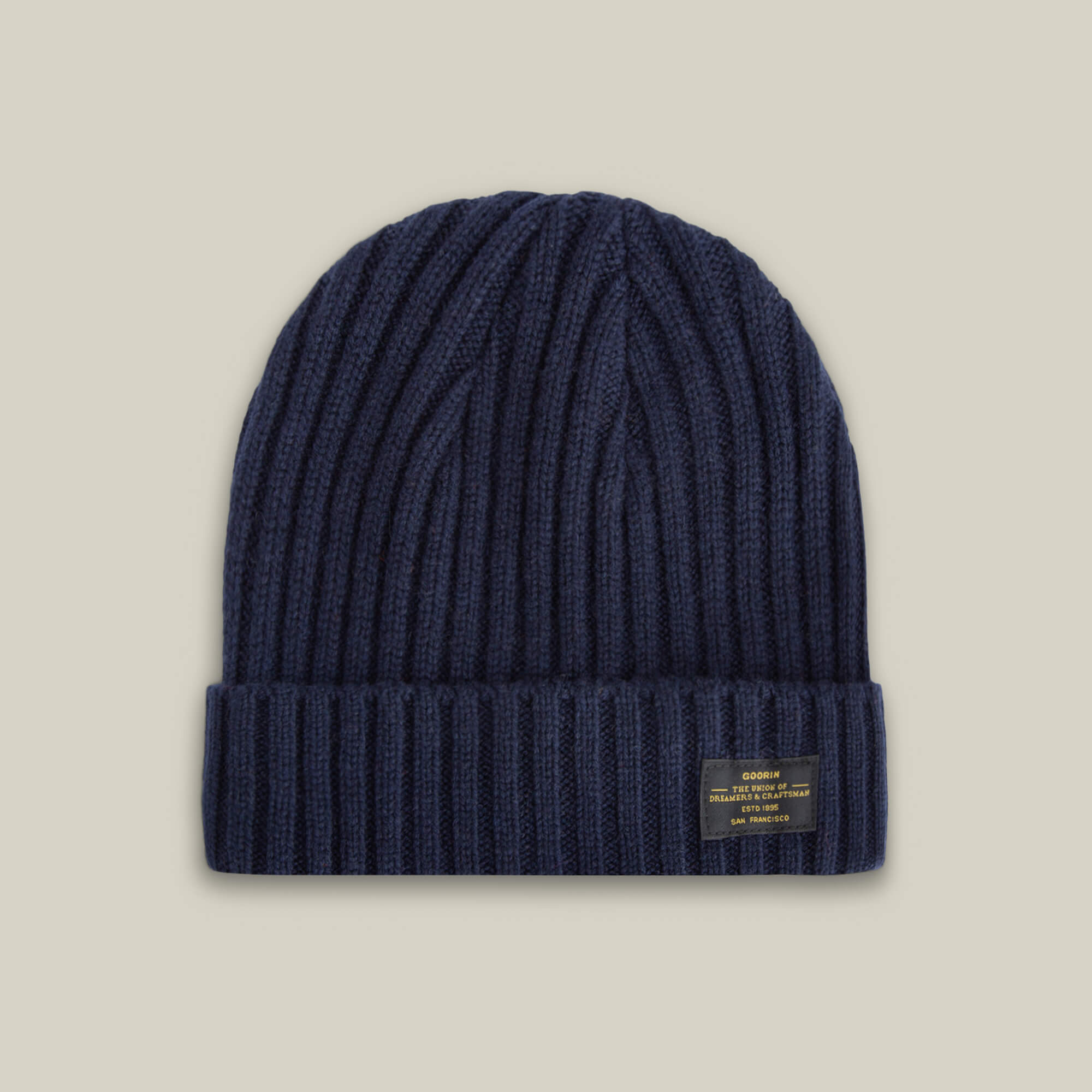 The Dream Cap by Goorin Bros. is a navy blue knitted beanie made from luxurious cashmere wool, featuring a ribbed texture, folded cuff, and a small rectangular front label, shown on a neutral background.