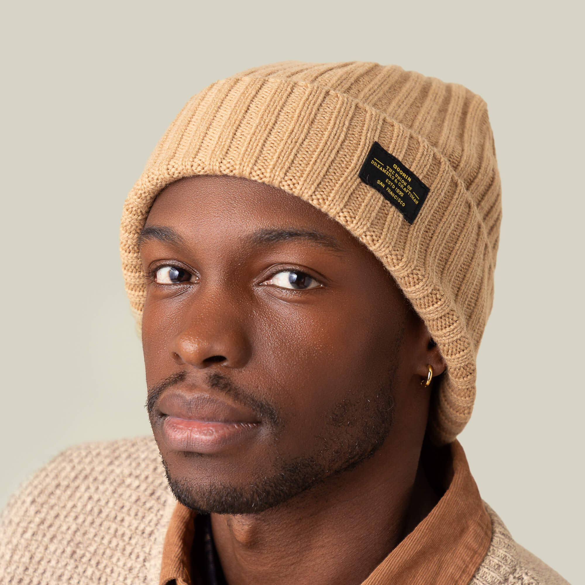 Wearing the Goorin Bros. Dream Cap, a luxurious beige knitted beanie, and a textured beige cashmere wool sweater, a person gazes at the camera with a neutral expression.