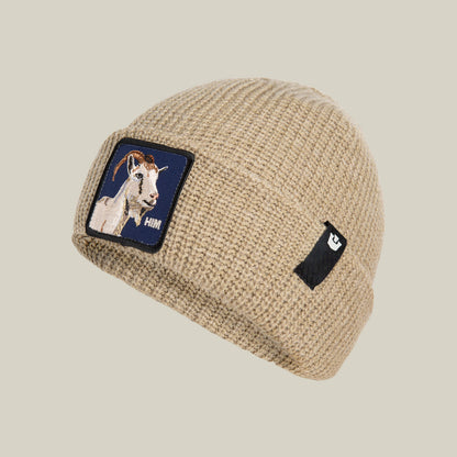 The Him Beanie by Goorin Bros. is a tan knit beanie featuring a playful goat patch with a white goat illustration and a small black patch displaying a white letter E.