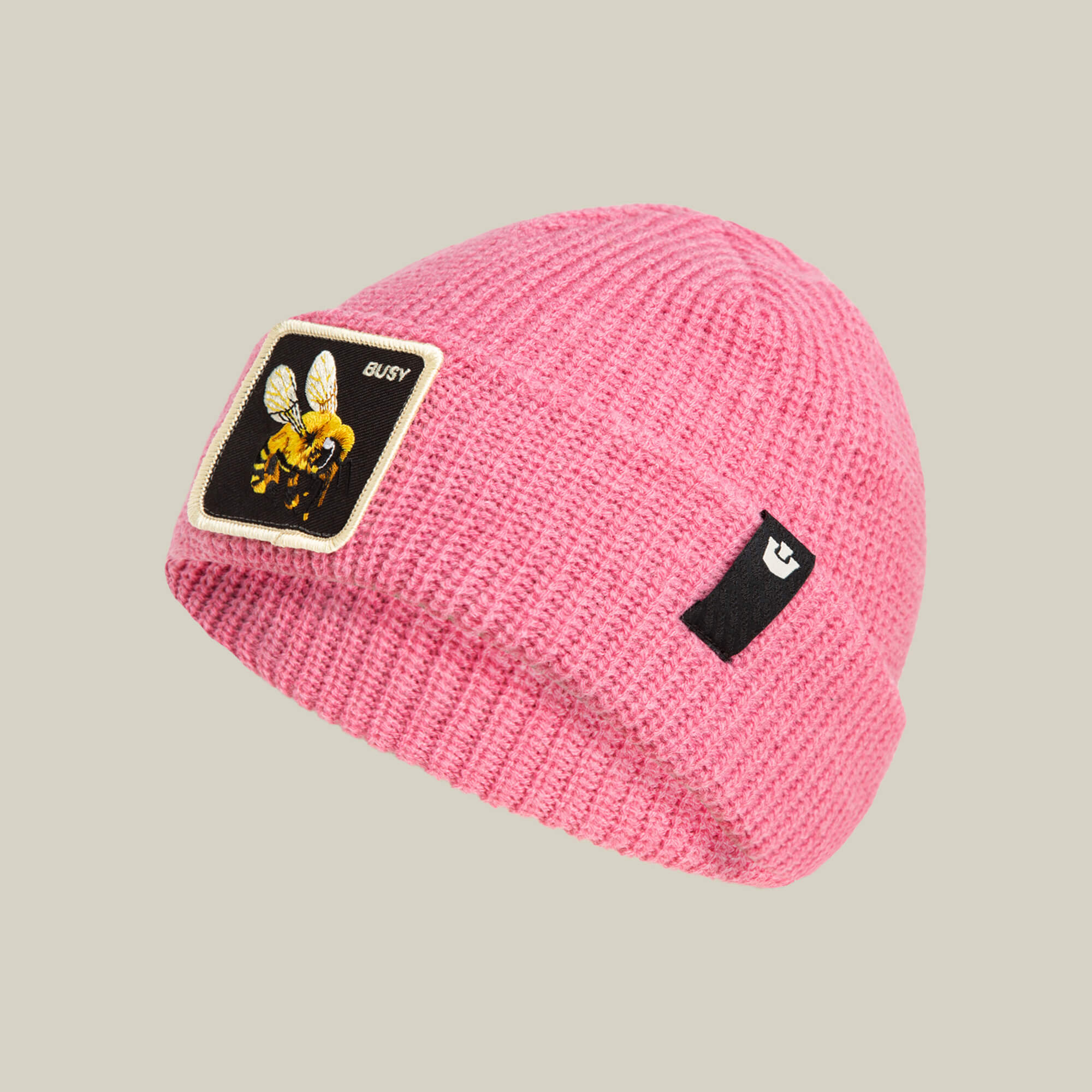The Busy Beanie by Goorin Bros. is a pop-pink knit hat featuring a buzzing bee patch with "BUSY" on the front and a small black logo tag on the side.