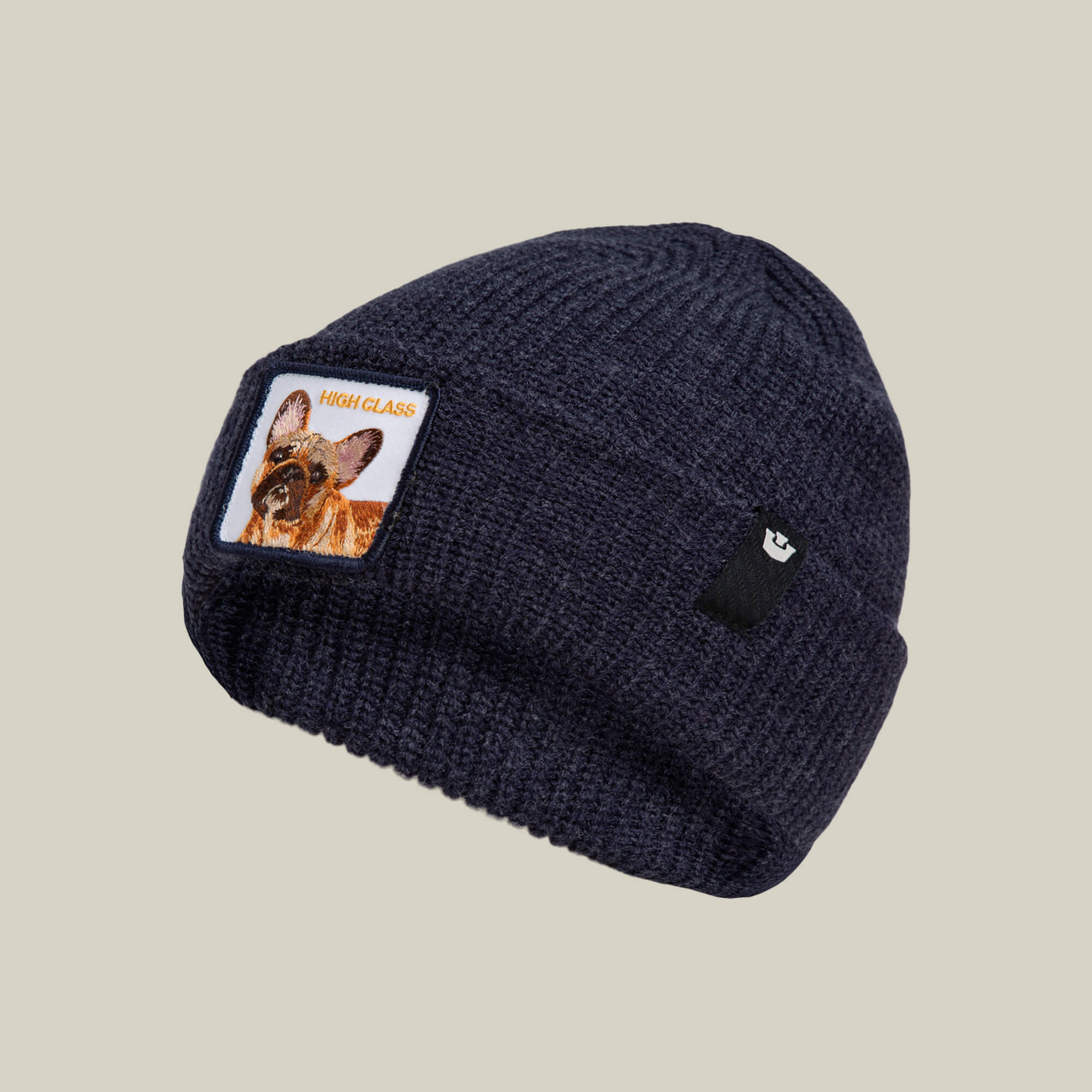 The High Class Beanie by Goorin Bros. is a navy knit winter hat featuring a dog patch and "HIGH CLASS" on the front, displayed against a plain beige background.