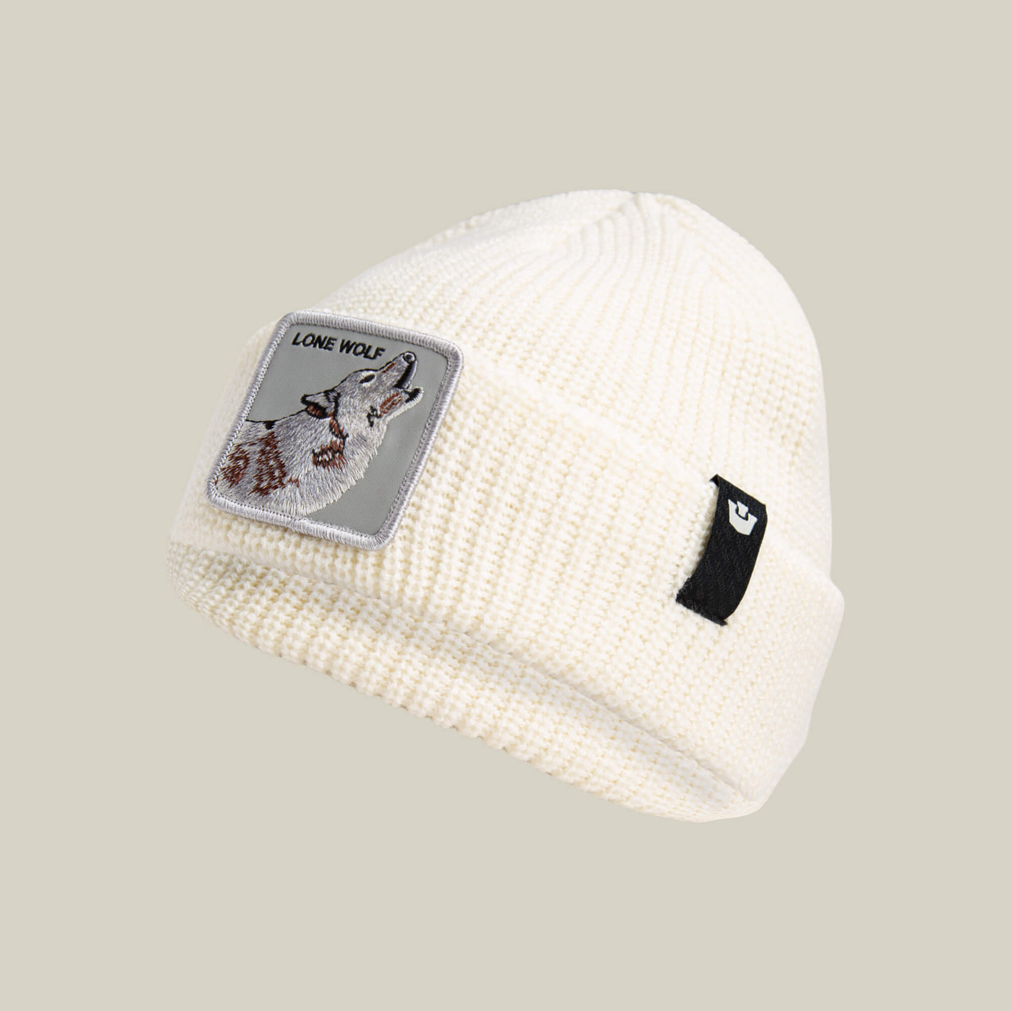 The Lone Wolf Beanie by Goorin Bros. is a white knit winter hat featuring a howling wolf patch labeled "LONE WOLF" and a small black tag on the cuff.