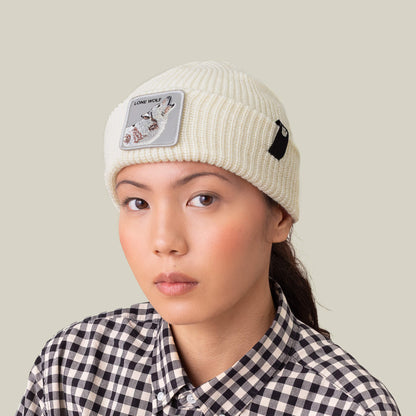 A person faces forward in the Goorin Bros. "The Lone Wolf Beanie," a cream winter hat featuring a howling wolf patch, paired with a black-and-white checkered shirt against a plain background.