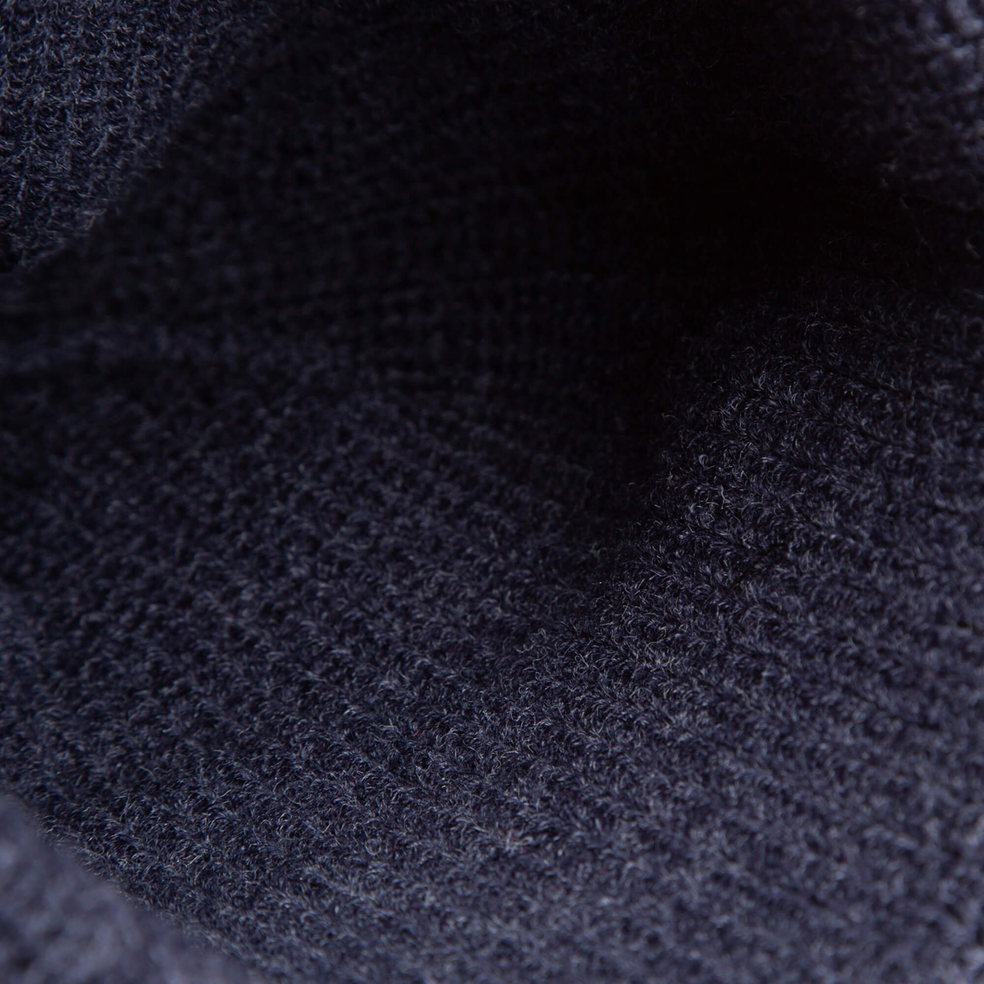 Close-up of dark navy knit fabric from The Top Beanie by Goorin Bros., showcasing its textured, woven pattern and fibers—beautifully accented with a signature St. Bernard patch.