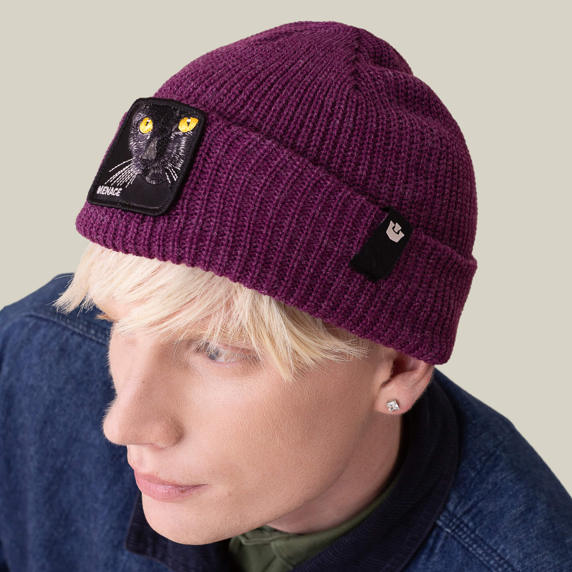 A person with light hair wears The Menace Beanie by Goorin Bros. in plum with a black cat patch and a denim jacket, looking upwards.