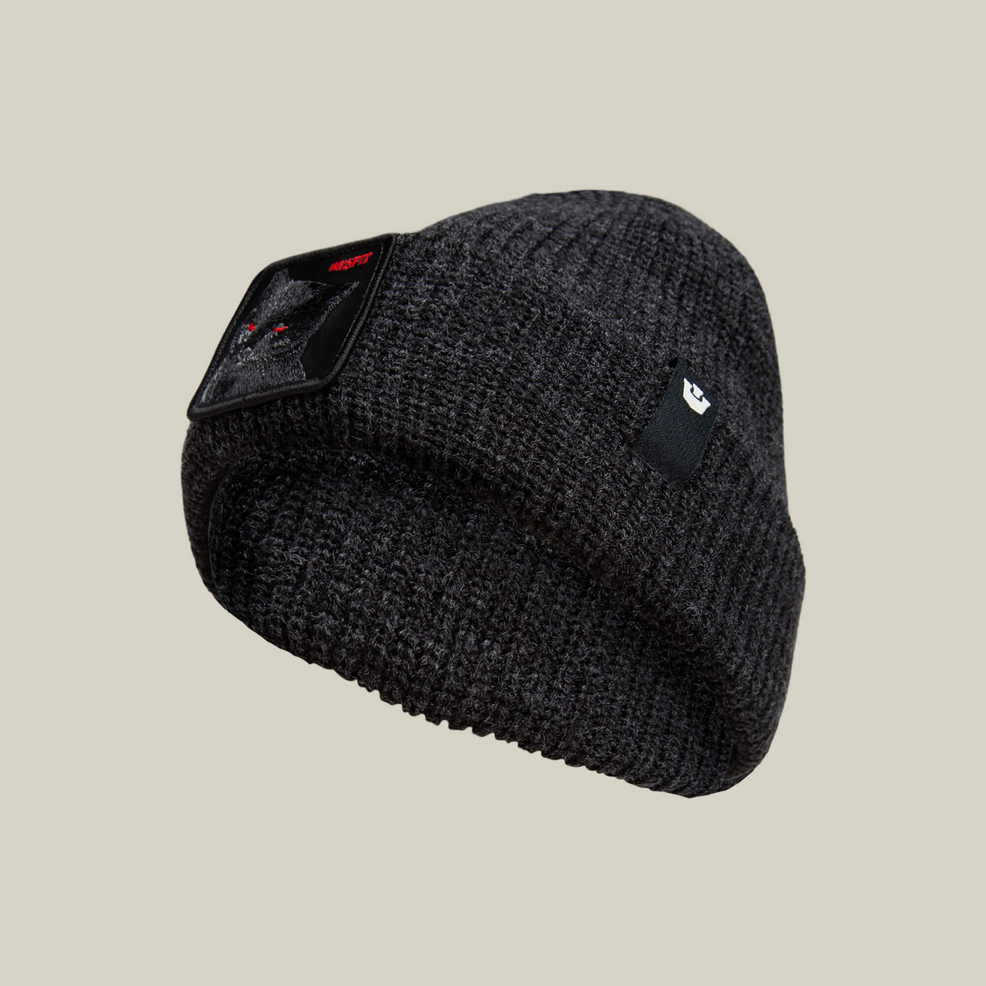 The Misfit Beanie by Goorin Bros. is a dark gray knit hat with a black rectangular cat patch featuring red eyes and text, plus a small black tag with a white logo on the folded brim.
