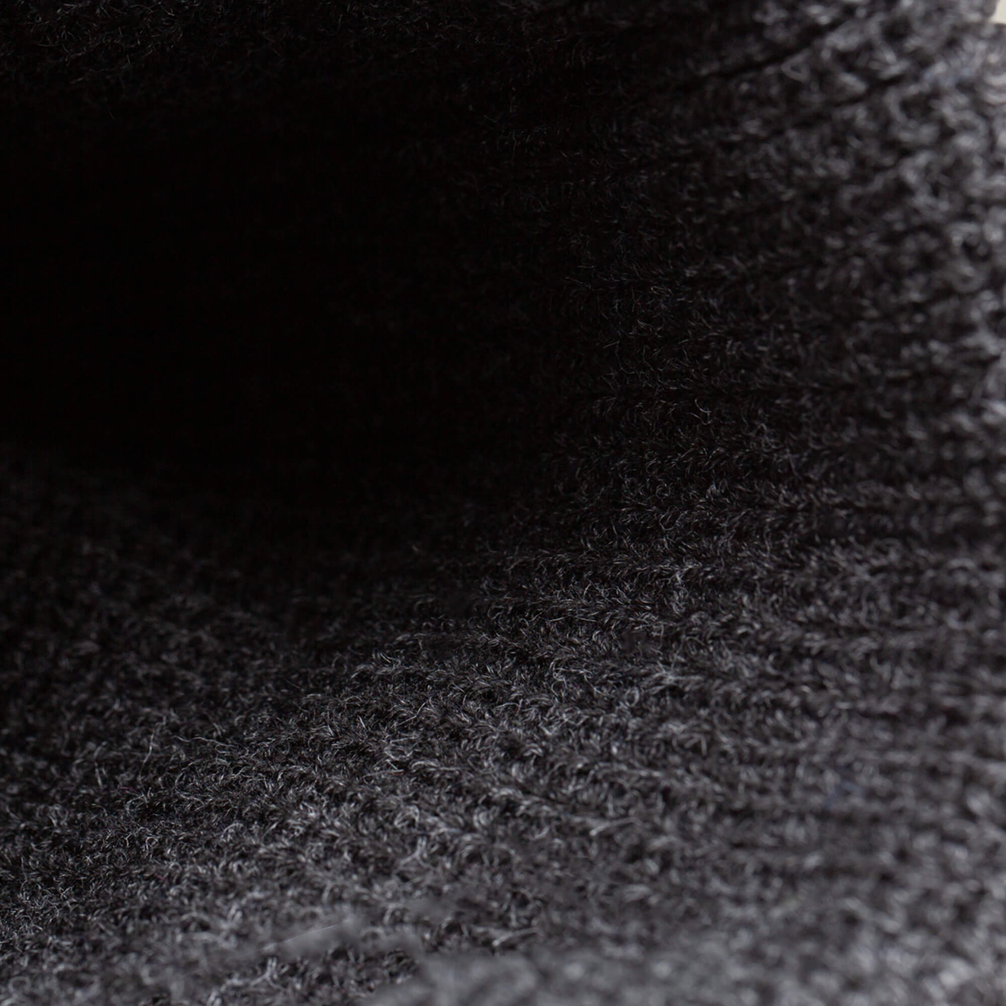 Close-up of The Lion Beanie by Goorin Bros., showing its heavyweight knit, dark textured fabric, and visible woven pattern highlighted by soft lighting.