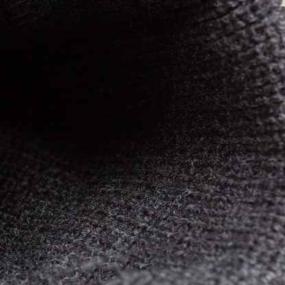 Close-up of The Lion Beanie by Goorin Bros., showing its heavyweight knit, dark textured fabric, and visible woven pattern highlighted by soft lighting.