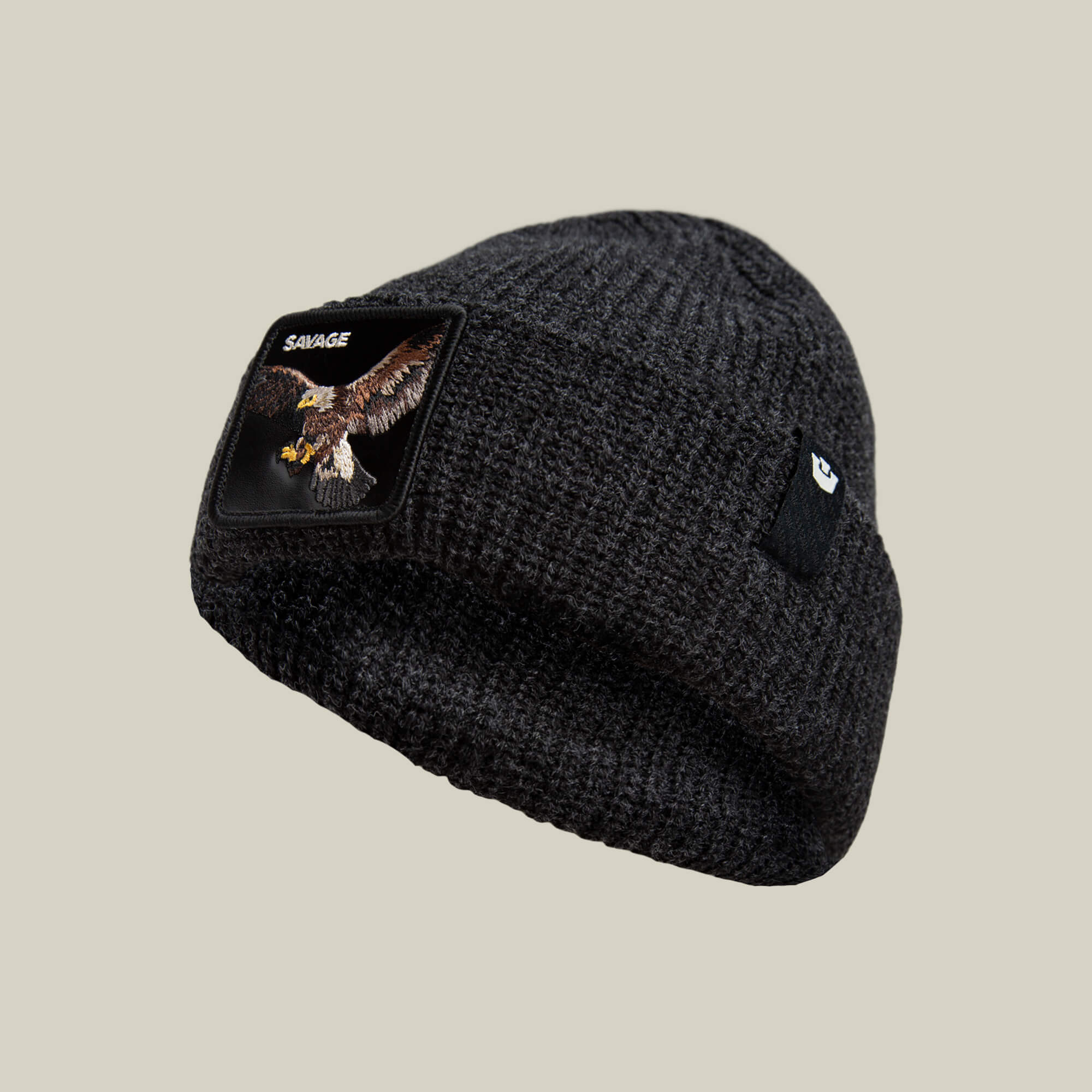 The Savage Beanie by Goorin Bros. is a warm, rugged dark knit beanie with an eagle patch, SAVAGE embroidery on one side, and a small black logo tag on the other.