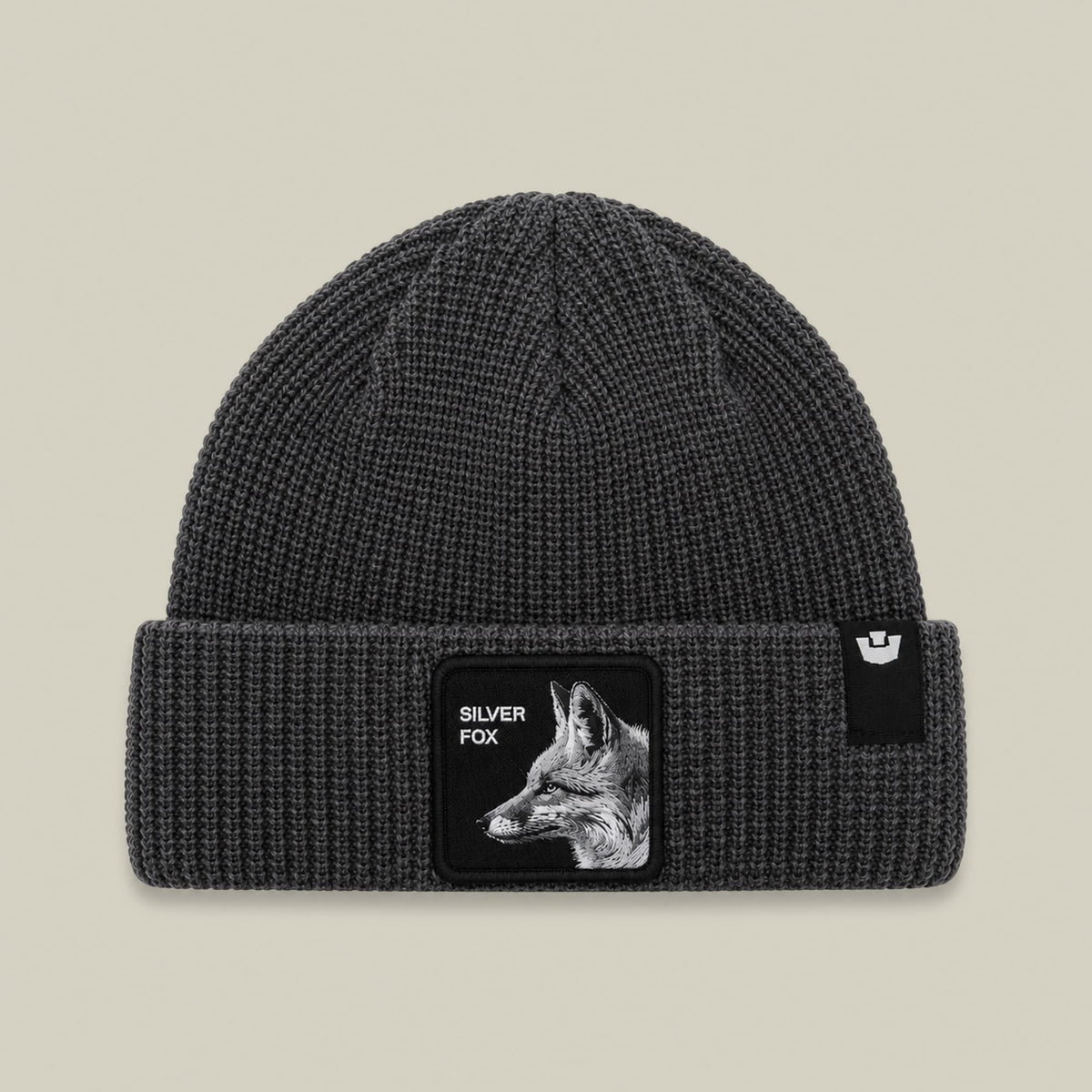 The Silver Beanie by Goorin Bros is a charcoal gray ribbed knit beanie with a black patch featuring a silver fox illustration and text on the front.