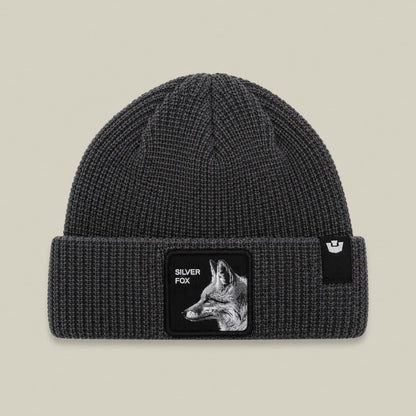 The Silver Beanie by Goorin Bros is a charcoal gray ribbed knit beanie with a black patch featuring a silver fox illustration and text on the front.