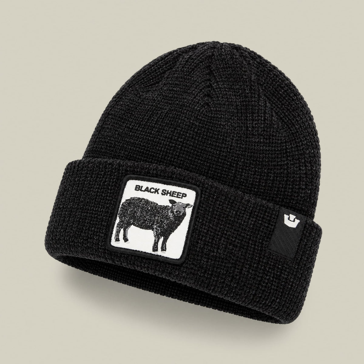 The Black Sheep Beanie by Goorin Bros is a black ribbed knit beanie with a white graphic patch featuring a black sheep illustration and text on the front, displayed against a neutral background.