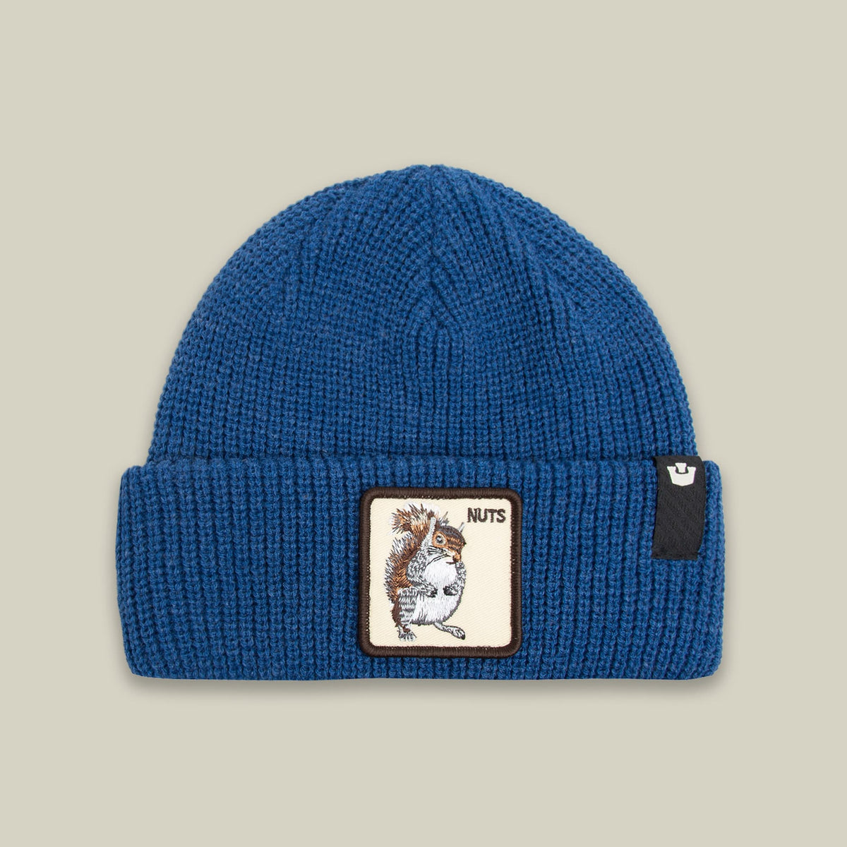 The Nuts Beanie by Goorin Bros. is a blue ribbed knit beanie featuring a brown and cream embroidered squirrel patch with "NUTS" text on the front, displayed against a neutral background.
